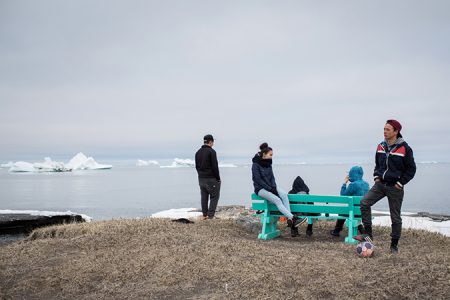 Jugendliche auf einer Bank in Queqertarsuaq, im Hintergrund Eisberge und Meer